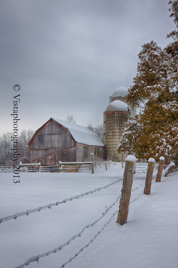 a barb wire fence leads the eye up to the next post to the trees and then the barn. Snow blankets everything with quiet.