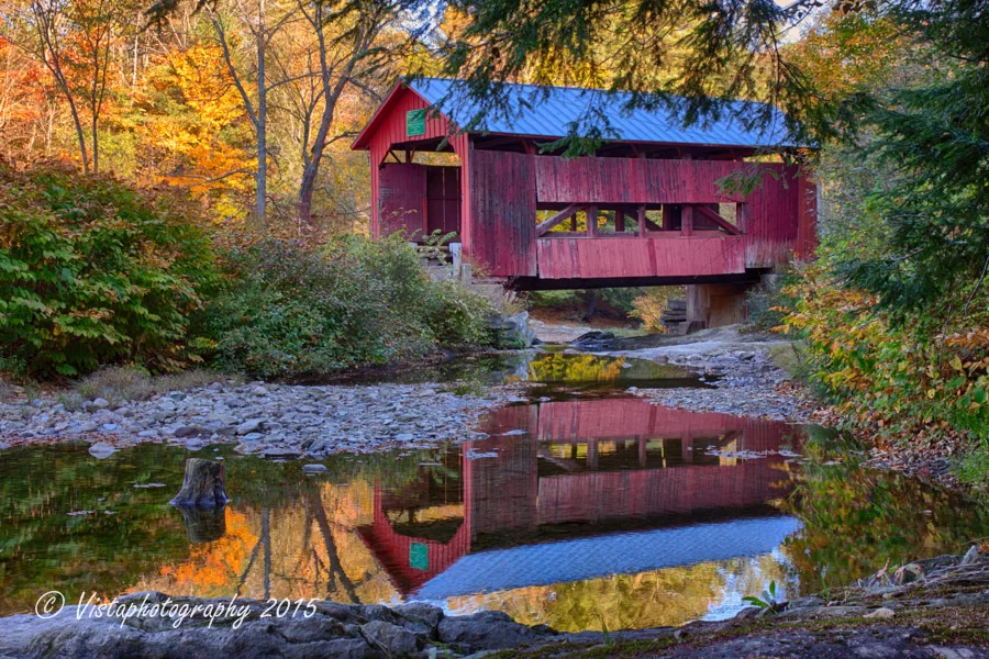 Upper Cox Brook Covered Bridge in autumn colors with a beautiful  reflection in the stream above it.