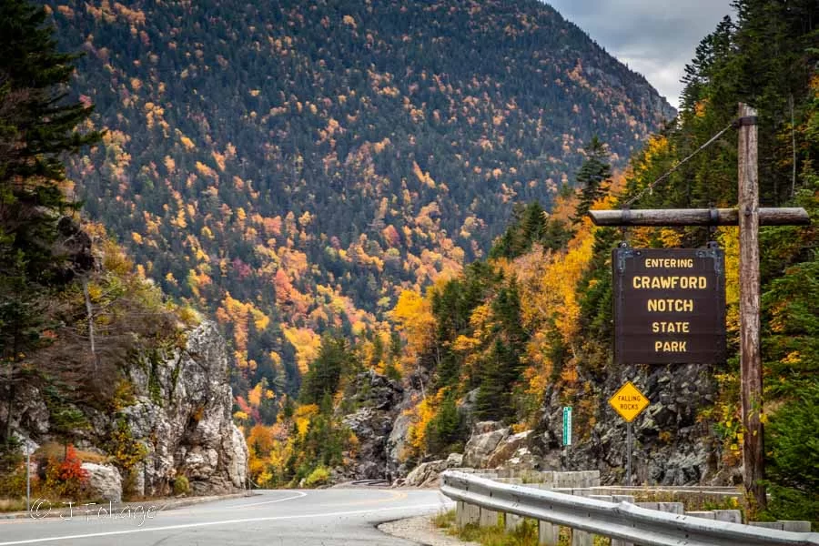 Entering Crawford Notch State Park sign with the orange and gold fall colors amid the pine trees