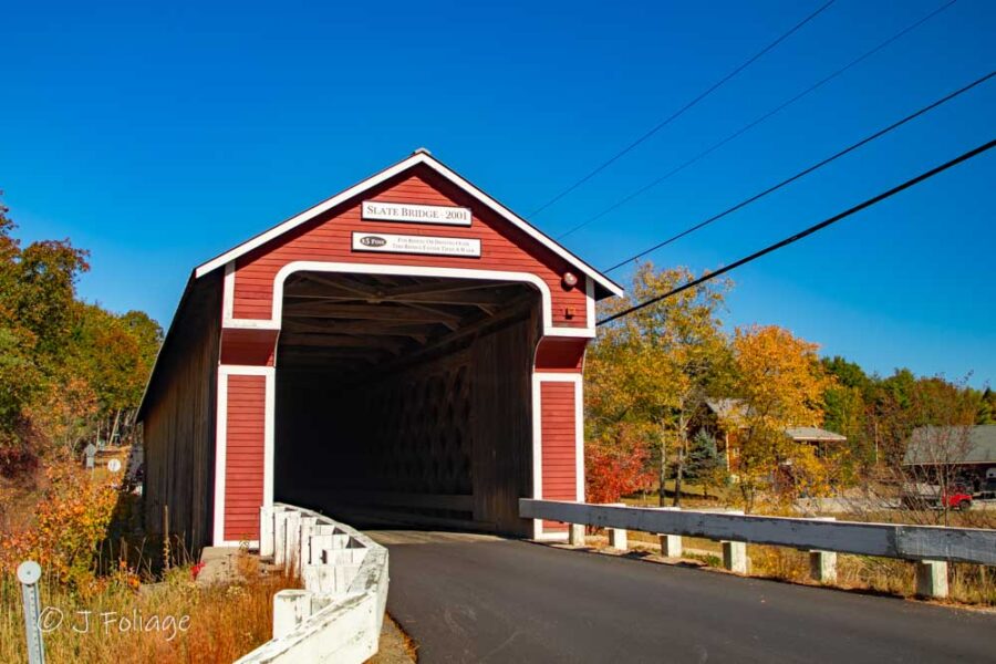 Rebuilt red Slate Covered Bridge with high clearance over the Ashuelot River during peak autumn color