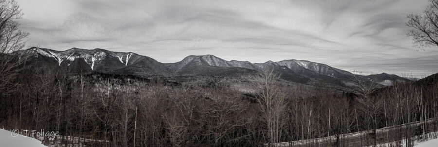 A White Mountains winter drive, stopping at the Hancock Scenic Vista: Wide-angle view of the hairpin turn on the Kancamagus Highway surrounded by bare winter trees and snow-dusted peaks.